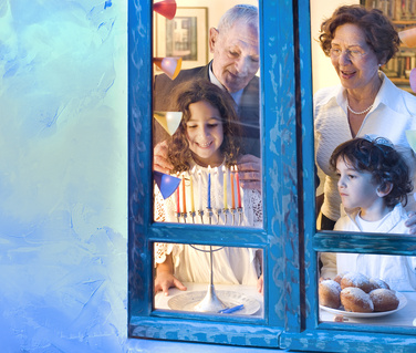a family lighting a chanukiah by the window